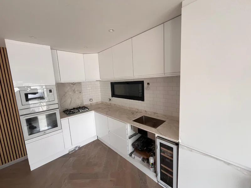 Cuisine en L, fa&ccedil;ades laqu&eacute;es sans poign&eacute;e, plan de travail effet marbre, colonne four et micro-ondes, chantier SFG B&acirc;ti Concept