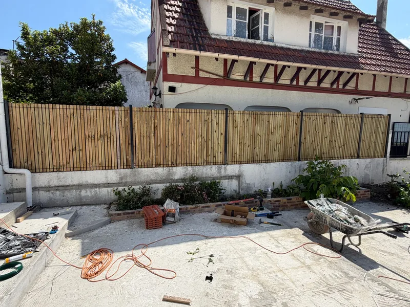 La m&ecirc;me cour ferm&eacute;e par une cl&ocirc;ture bois &agrave; lames verticales sur poteaux acier