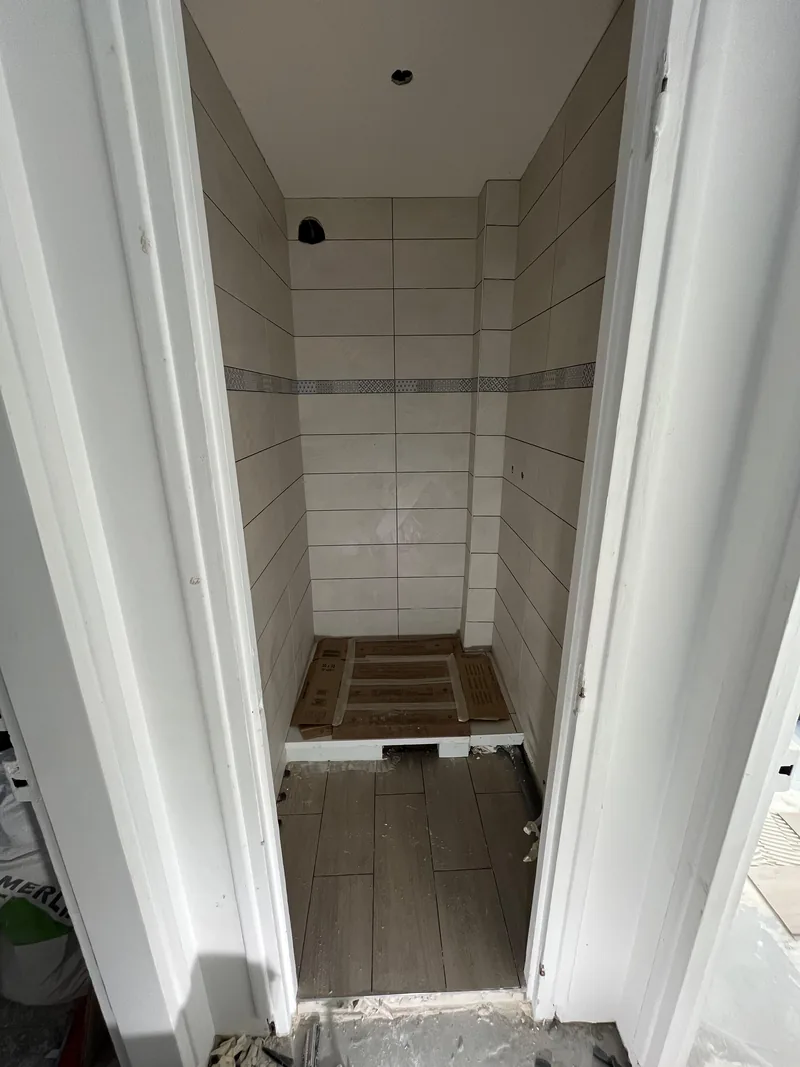 Salle d&rsquo;eau livr&eacute;e&nbsp;: fa&iuml;ence blanche grand format, frise en mosa&iuml;que et sol en carrelage imitation bois, chantier SFG B&acirc;ti Concept